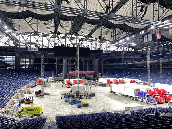 Ford Field being setup for a concert. Multiple semi trucks are parked in front of a stage that is being erected for an upcoming event